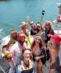 Lively boat party on blue water: group of friends in colorful swimwear, sunglasses and hats raising drinks and smiling on a sunny summer day.