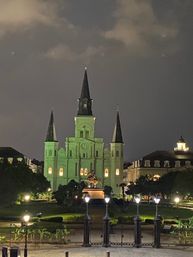 Historic St. Louis Cathedral in New Orleans’ Jackson Square, glowing green at night with three spires, an equestrian statue in front and lit lampposts in the foreground.