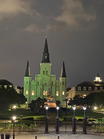 Historic St. Louis Cathedral in New Orleans’ Jackson Square, glowing green at night with three spires, an equestrian statue in front and lit lampposts in the foreground.