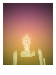 Seated woman portrait with a gentle smile against a purple-to-gold gradient light-leak backdrop, vintage film-style effect, wearing a black top and delicate necklace.