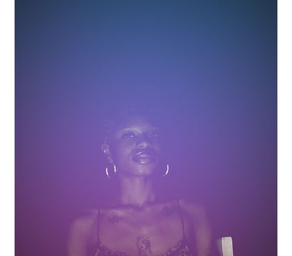 Moody night portrait of a woman bathed in purple-blue neon light, wearing hoop earrings and a patterned spaghetti-strap top with visible chest tattoos against a dark background.