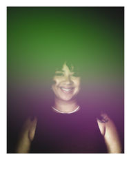 Smiling person in a dark sleeveless top and delicate necklace, curly hair framing their face, dreamy green-to-purple gradient overlay across the portrait.