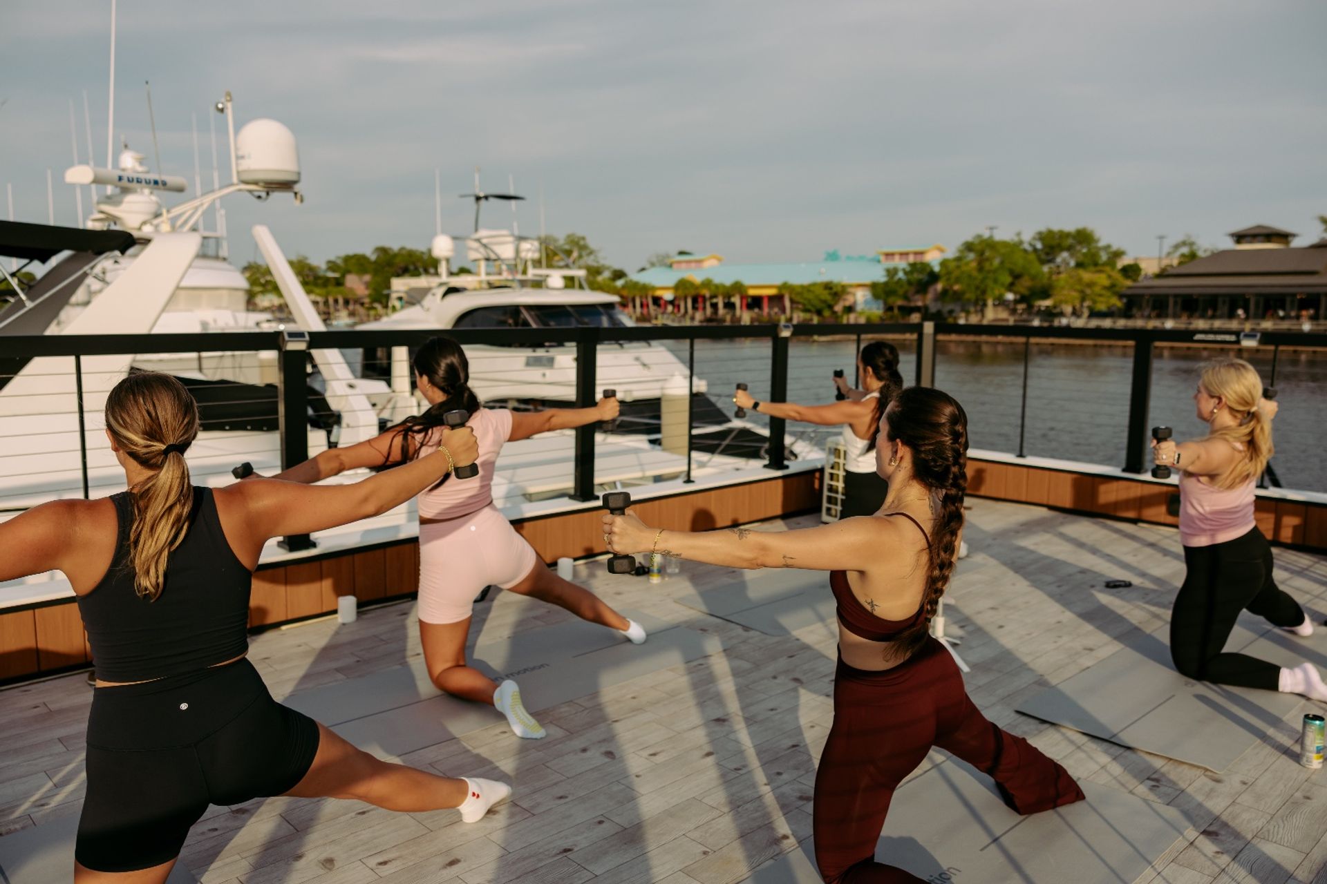 Group of women powering through a waterfront dumbbell workout on a marina deck with yachts and calm water in the background.