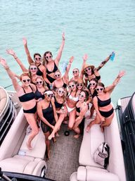 Group of women in swimsuits wearing heart-shaped sunglasses cheering on a pontoon boat over clear turquoise water — summer boat party, girls’ getaway.