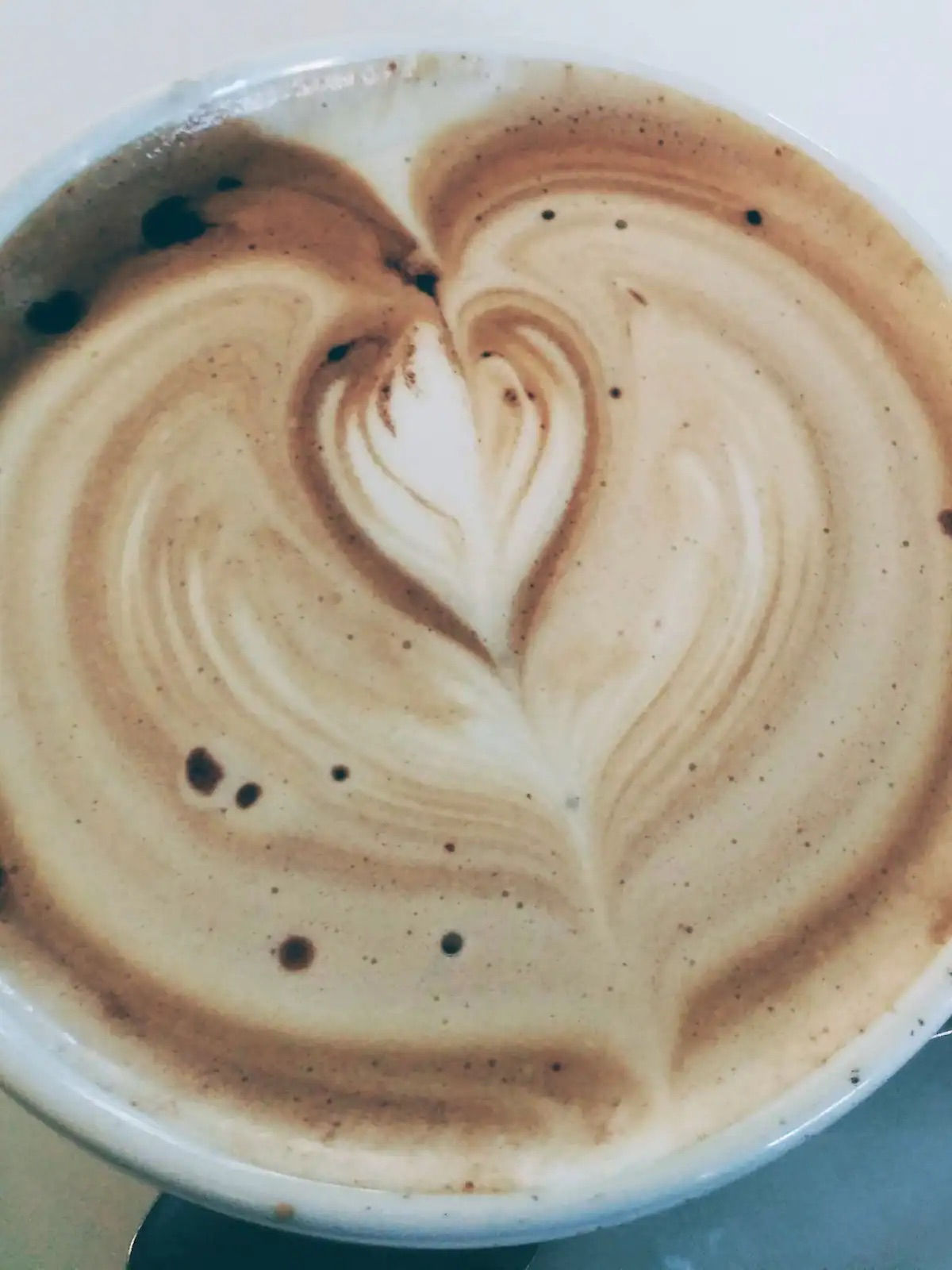 Top-down close-up of a latte in a white cup showing heart-shaped latte art, creamy espresso swirls, and small crema bubbles.