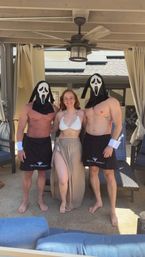 Poolside cabana party: smiling woman in a white bikini flanked by two shirtless men in pinstripe aprons wearing ghost-face masks.