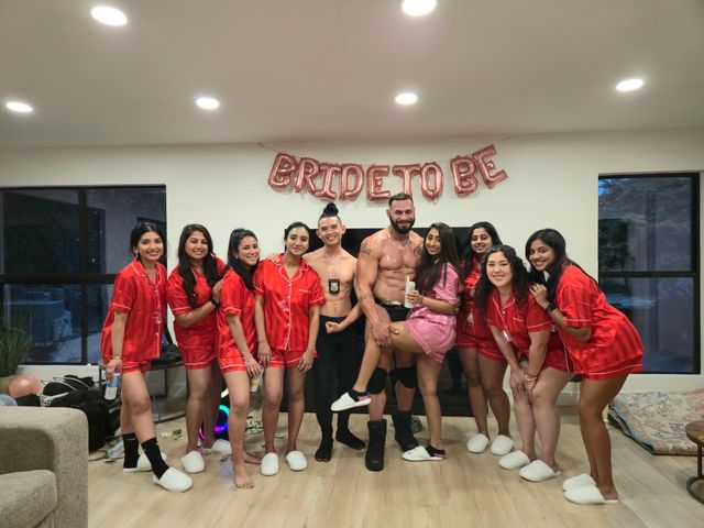 Bachelorette party group photo in a living room: women in matching red pajama sets and one in pink pose with two men under rose-gold "BRIDE TO BE" balloons.
