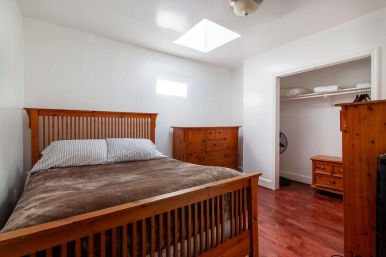 Cozy minimalist bedroom interior with wooden slatted bed, matching dresser and nightstand, skylight above, open closet and warm hardwood floors