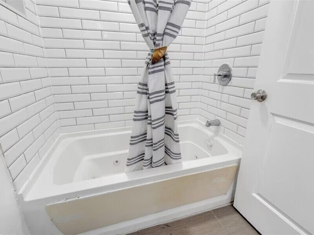 Modern residential bathroom with white subway-tile walls, a white jetted bathtub, chrome faucet and fixtures, and a gray-and-white striped shower curtain tied in the center
