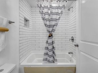 Bright white subway-tile bathroom with a bathtub, built-in niche, chrome fixtures, and a gray-striped shower curtain tied in the center