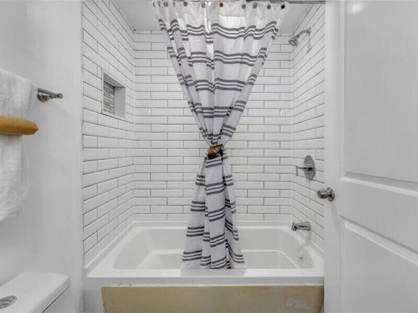 Bright white subway-tile bathroom with a bathtub, built-in niche, chrome fixtures, and a gray-striped shower curtain tied in the center