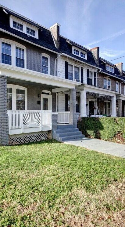 Gray brick row houses with covered front porches, dormer windows and trimmed hedges along a tree-lined sidewalk in an urban residential neighborhood