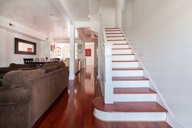 Open-plan living room and foyer with a white staircase featuring dark wood treads, glossy hardwood floors, brown sectional sofa and dining area
