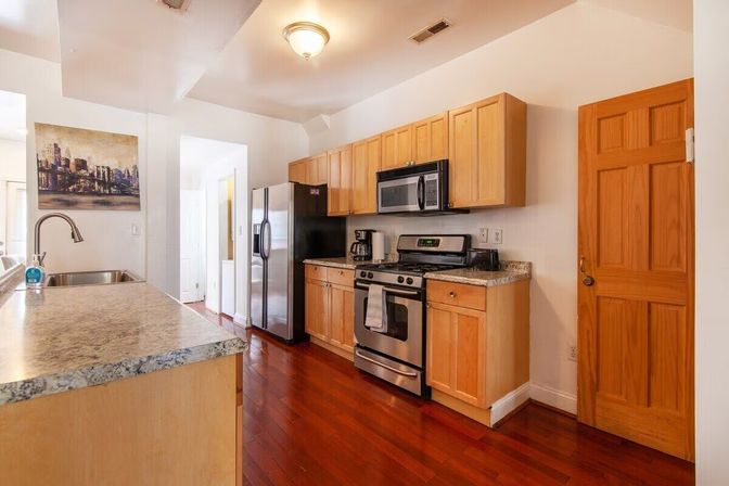 Bright modern kitchen with stainless steel refrigerator, gas range and microwave, light wood cabinets, granite countertops, island sink and polished hardwood floors.