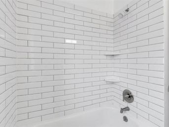 Crisp white subway-tile bathtub and shower with chrome faucet, wall-mounted showerhead and built-in corner shelves, modern clean bathroom