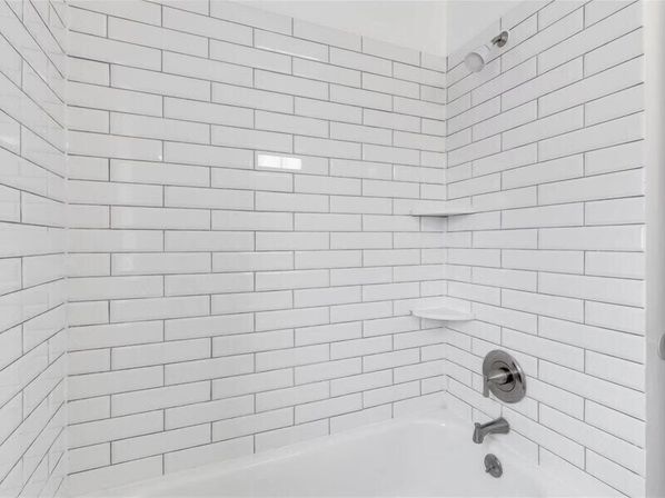 Crisp white subway-tile bathtub and shower with chrome faucet, wall-mounted showerhead and built-in corner shelves, modern clean bathroom