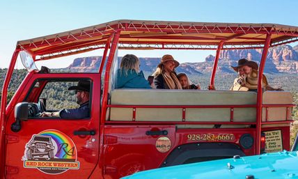 Open-air red jeep with smiling passengers in cowboy hats enjoying a scenic Sedona, Arizona red-rock landscape under a clear blue sky.