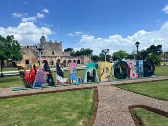 Bright, hand-painted VALLADOLID letters on a grassy plaza with a historic stone convent and blue sky in Valladolid, Yucatán, Mexico