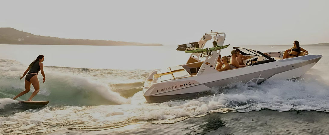 Wakesurfer carving a wake behind a white speedboat as passengers relax, cruising across sunlit coastal waters at golden hour.
