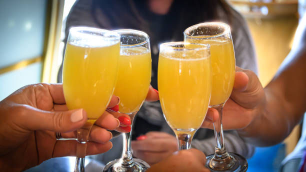 Four hands clinking champagne flutes filled with bright orange mimosas in a festive brunch toast