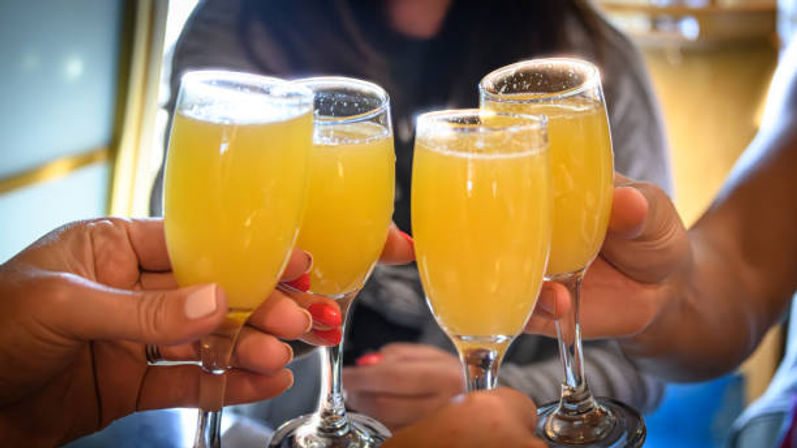 Four hands clinking champagne flutes filled with bright orange mimosas in a festive brunch toast