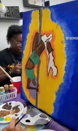 Artist in a paint studio creating a vibrant acrylic canvas of a pole-dancer silhouette against blue, orange, and yellow background, with paint palette, brushes and bottles on the table.