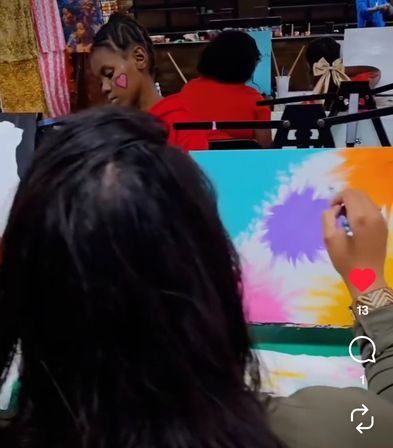 Children's painting workshop in an art studio — close-up of a person painting a bright turquoise, purple and orange canvas while another child with a pink heart face paint works at an easel.