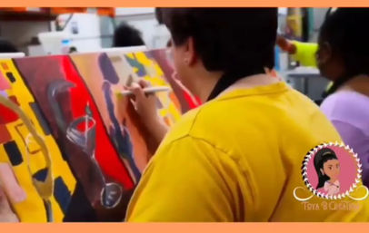 Person in a yellow shirt painting a vibrant abstract canvas during a lively group art class in an indoor studio