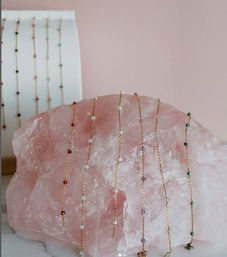 Delicate gold-chain beaded bracelets with tiny multicolored gemstone beads draped over a large rose quartz slab on a soft pink backdrop.