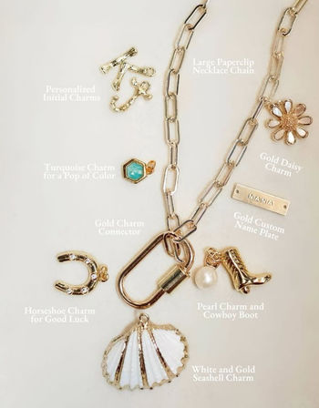 Gold paperclip chain jewelry flatlay with white-and-gold seashell pendant, pearl and cowboy boot charms, daisy, horseshoe, turquoise hex and personalized name plate — beach-inspired charm necklace