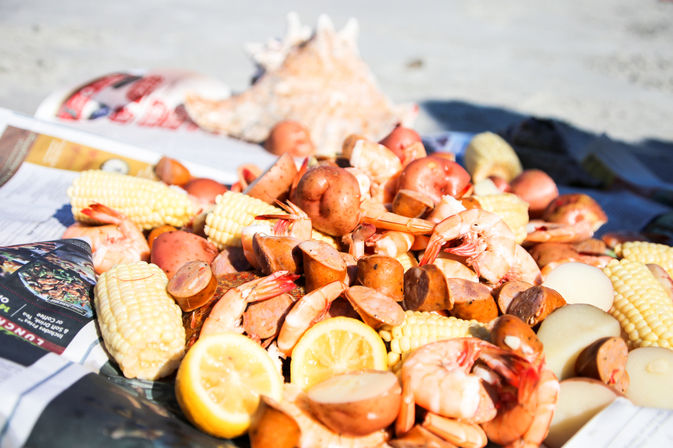 Beach picnic shrimp boil piled on newspaper with boiled shrimp, corn on the cob, red potatoes, smoked sausage and lemon wedges