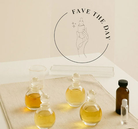 Minimalist flatlay of round glass perfume/serum bottles and amber vials holding golden facial oils on linen, set against a beige studio backdrop with a circular “FAVE THE DAY” graphic.