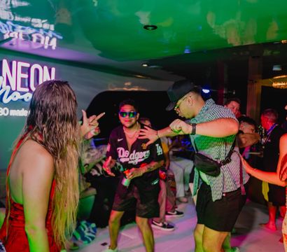 People dancing and laughing under neon lights on a lively Cabo boat party with colorful club-style atmosphere