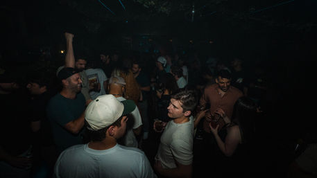 Crowded dim indoor nightclub with people holding drinks, dancing and chatting, lively urban nightlife vibe