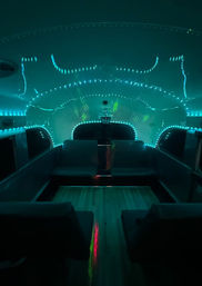 Teal LED-lit retro travel trailer interior with U-shaped bench seating, wood floor and disco-ball light reflections creating a futuristic glamping lounge vibe.