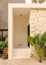 Minimalist outdoor plunge bath alcove with neutral stucco, textured stone wall and lush tropical plants