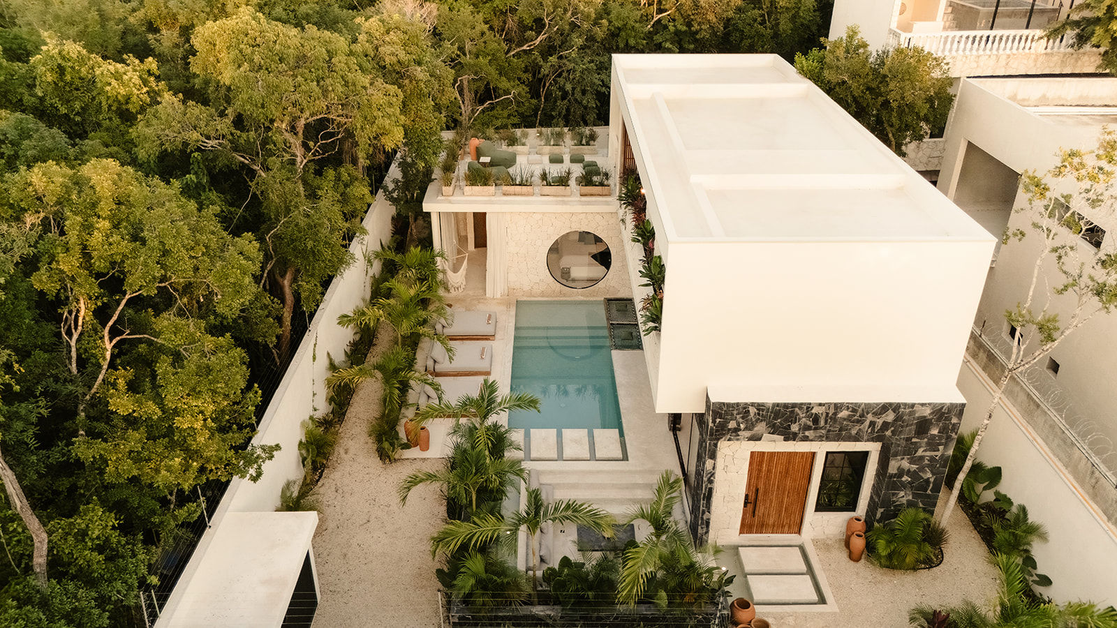 Aerial view of a modern white villa with rooftop terrace and rectangular plunge pool, framed by palm landscaping and dense tropical forest.