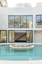 Modern minimalist white villa with turquoise pool, circular sunken lounge island, floor-to-ceiling windows, floating staircase and reflected trees
