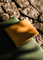 Sunlit orange notebook on a green seat cushion set against textured cobblestone, warm shadows across the cover.