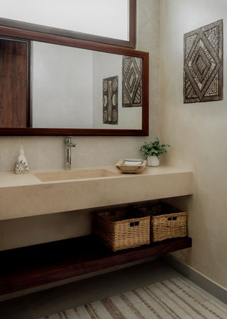 Spa-like neutral bathroom vanity with integrated beige stone sink, wood-framed mirror, chrome faucet, wicker storage baskets on a dark wood shelf, small potted plant and geometric wall art