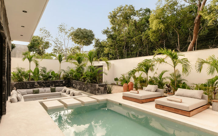 Modern tropical villa pool patio with turquoise pool, stepping stones, sunken cushioned lounge and wooden daybeds framed by palm plants and a privacy wall