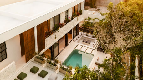 Bird's-eye view of a modern luxury villa courtyard with a turquoise plunge pool, stepping-stone entry, sunken outdoor lounge with cushioned seating, planters and tropical landscaping.