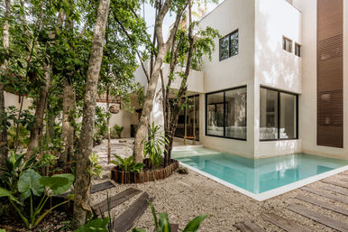 Modern white villa courtyard with turquoise plunge pool, floor-to-ceiling windows, lush tropical trees, gravel paths and wooden stepping stones — a private oasis.