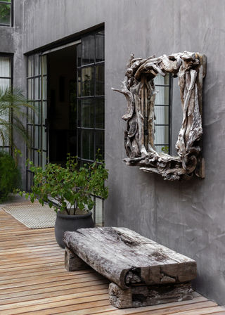 Weathered driftwood mirror and reclaimed wood bench on a modern gray concrete patio with potted plant and industrial-style glass doors