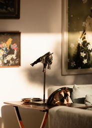 Sunlit living room side table with a bronze bull sculpture on a stand, carved wooden animal mask with fangs, metal tray and framed artwork