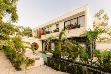 Modern two-story tropical villa with private pool, lush palm landscaping, stone facade, large windows and outdoor lounge with terracotta pots.