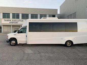 White passenger shuttle parked on tarmac outside a sleek executive airport terminal with large tinted windows reflecting the sunset.