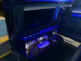 Luxury limo interior at night with blue LED mood lighting, built-in bar with glassware and cup holders, and black leather seating