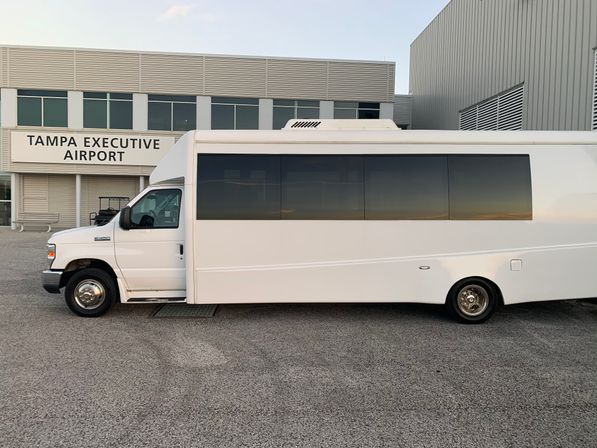 White passenger shuttle with tinted windows parked outside an executive airport terminal in Tampa on a pastel sunset tarmac.
