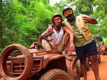 Two friends wearing goggles and bandanas pose on muddy ATVs on a lush forest trail after an off‑road mud ride — outdoor adventure photo.